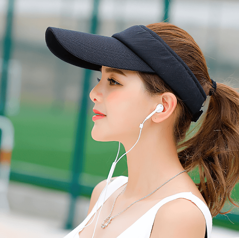 Woman wearing black adjustable tennis golf visor cap with UV protection, listening to music outdoors. Perfect for sports activities.